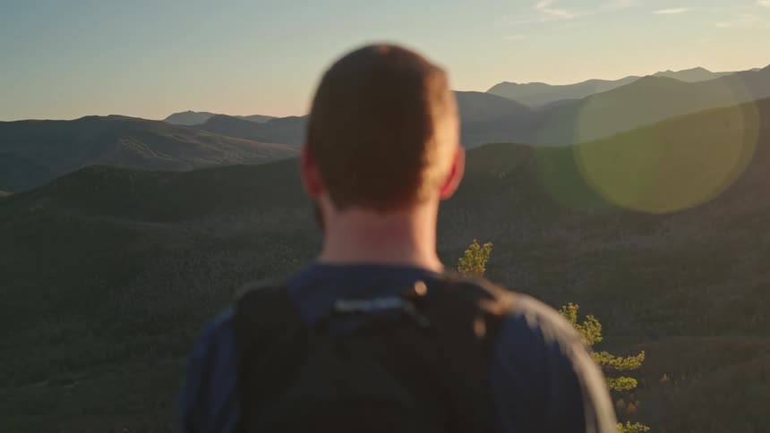 Man with a backpack stand facing the mountains at midday