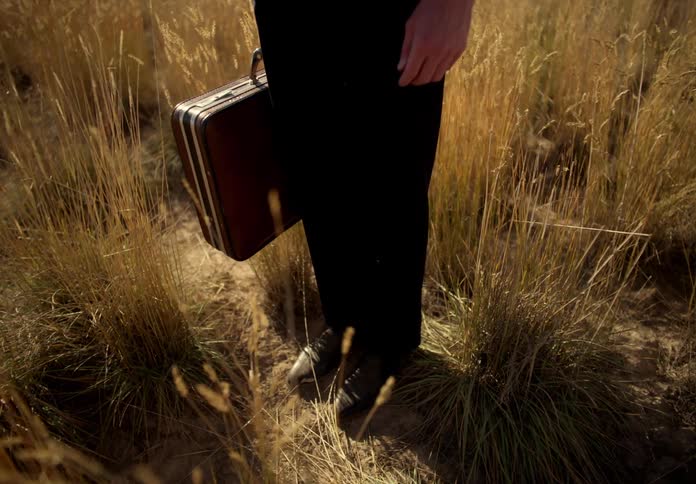 Man in a suit standing in a pasture holding a leather briefcase