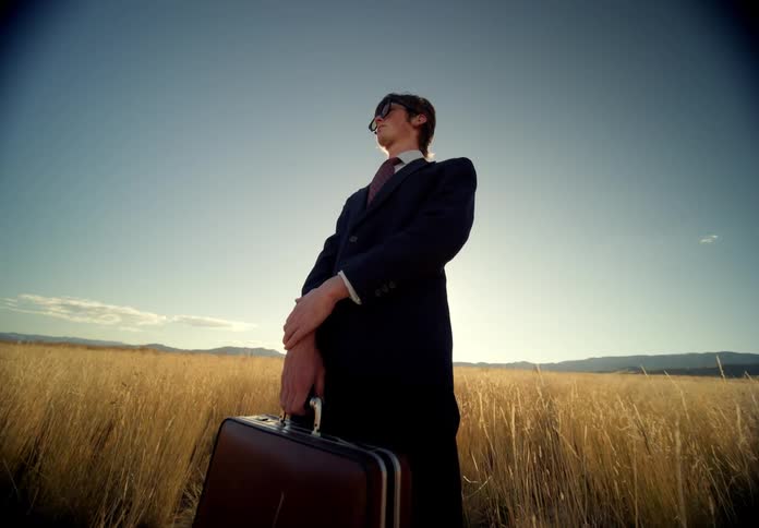 A man holding a suitcase while standing in a grassland in the middle of the wilderness