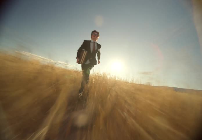 Man in formal attire suit and tie holding a briefcase and chaotically running in tall grass