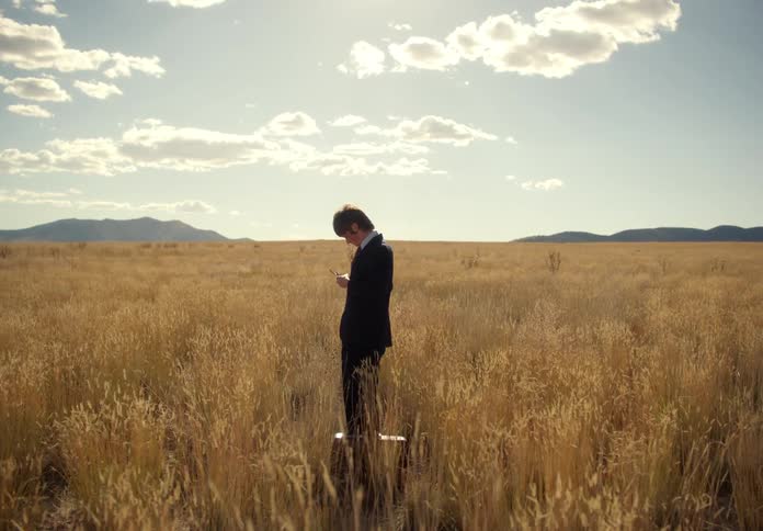 Businessman in suit and sunglasses stands in a field carrying a briefcase
