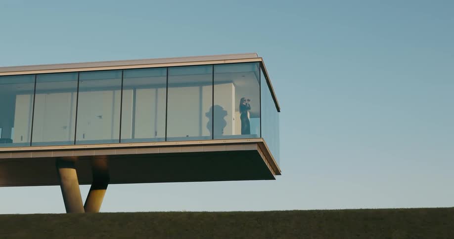 Exterior architecture of a mansion in the countryside with a woman inside the house observing the view with binoculars