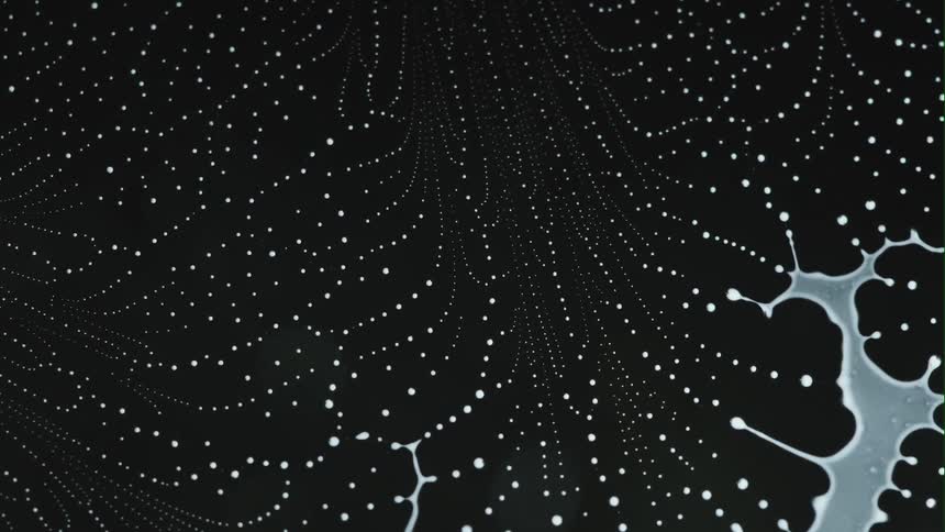 Abstract milky white liquid splashing on black surface then separating into webbed dot lines