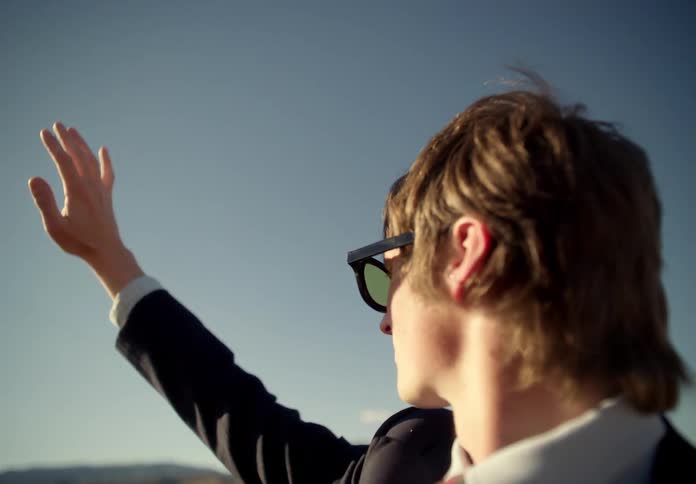 A man in a suit and sunglasses placing his hand in the bright sunlight