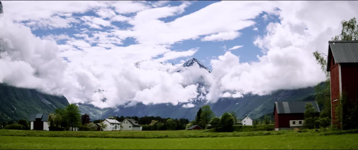 Landscape of a rural area with houses and mountain ranges on the horizon with clouds passing in time lapse