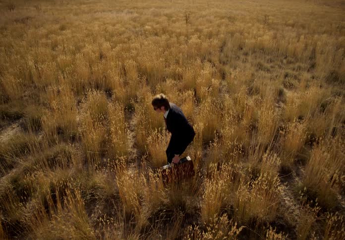 A man walking through the field with a briefcase in his hand