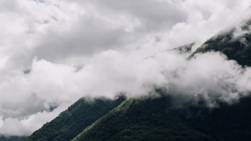 Clouds roll over forest covered hill top mountain peaks