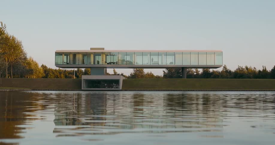 A modern building balances on two legs with a lower entrance leading to the lake