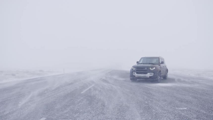 A car is parked in the middle of the road during a blizzard in the daytime