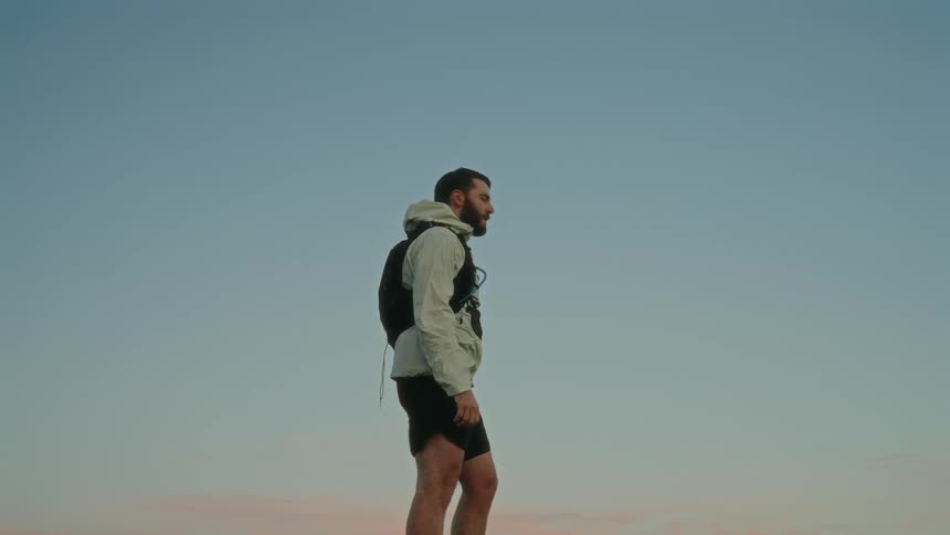 Man in shorts and a jacket with a backpack under an open sky in the morning