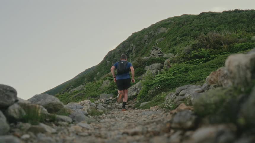 Man running along a trail under the mountains on a cloudy day