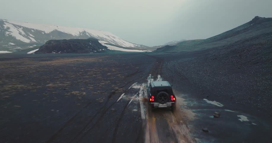 A black suv bounces along a rough muddy dirt track towards snowcapped rocky mountains