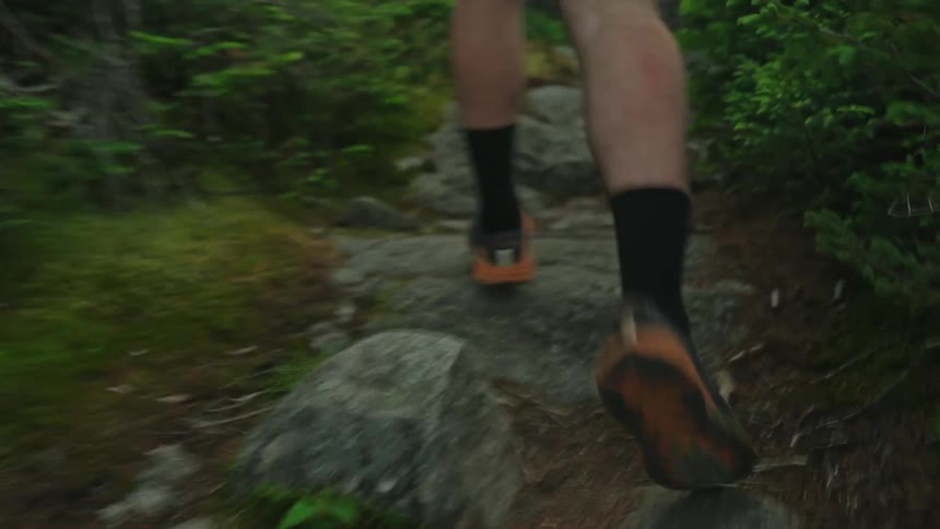 Man wearing black shorts socks and sneakers runs along a dirt track in the forest