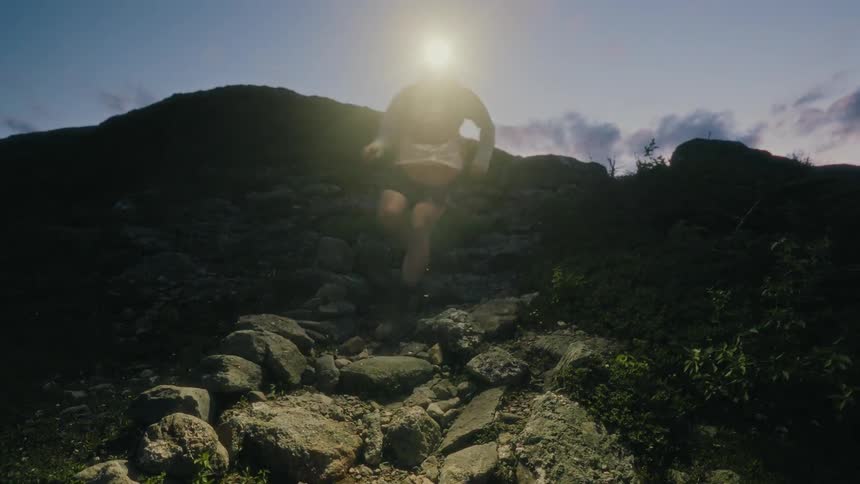 A man wearing a headlamp runs down a mountain path