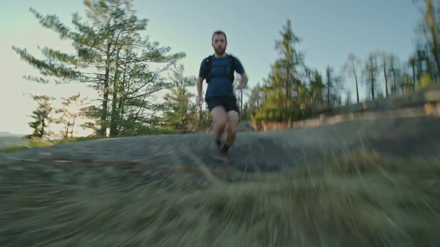 A man runs down a hill with trees in the distance
