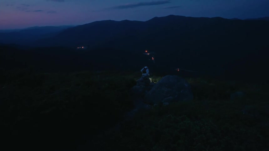 A man is running down a mountain trail while holding a flashlight on an early morning