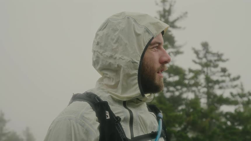 Hiker standing near conifers on a foggy day pulls up his hood