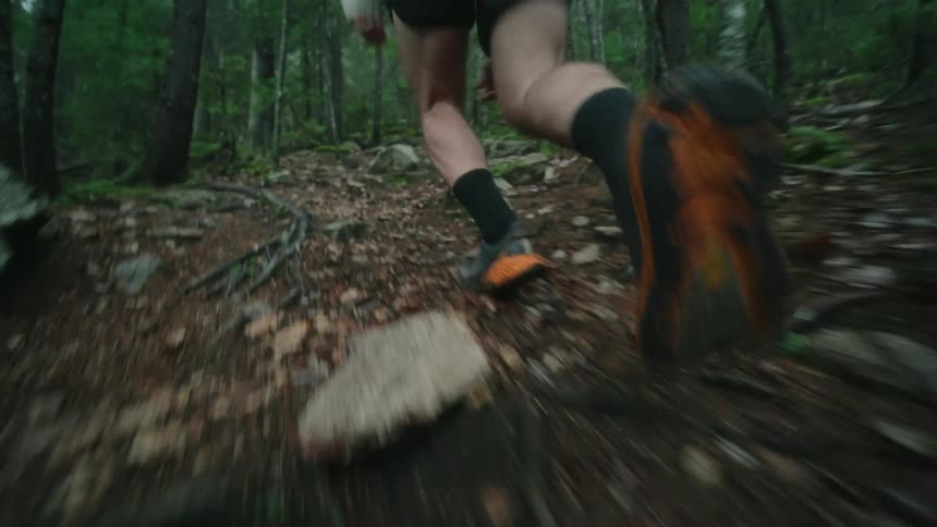 Closeup on the feet of a person running uphill in the middle of a forest