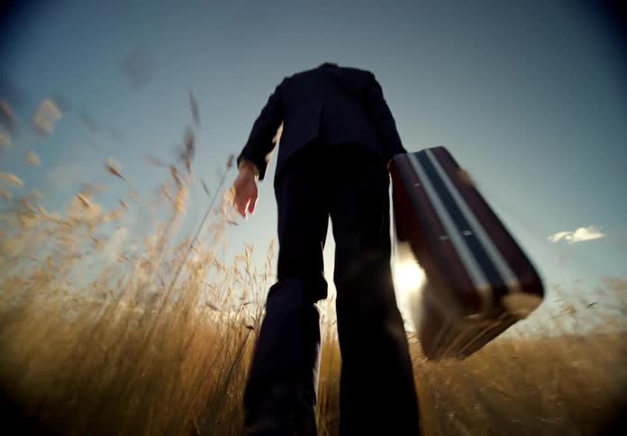 Man walking through a field of tall grass wearing a suit and holding a briefcase