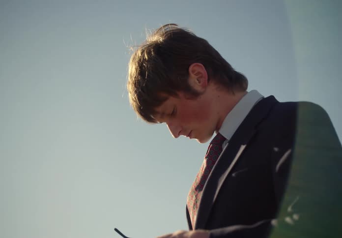 Man in a suit with a handbag cleaning his glasses looking at the sky and walking through a pasture