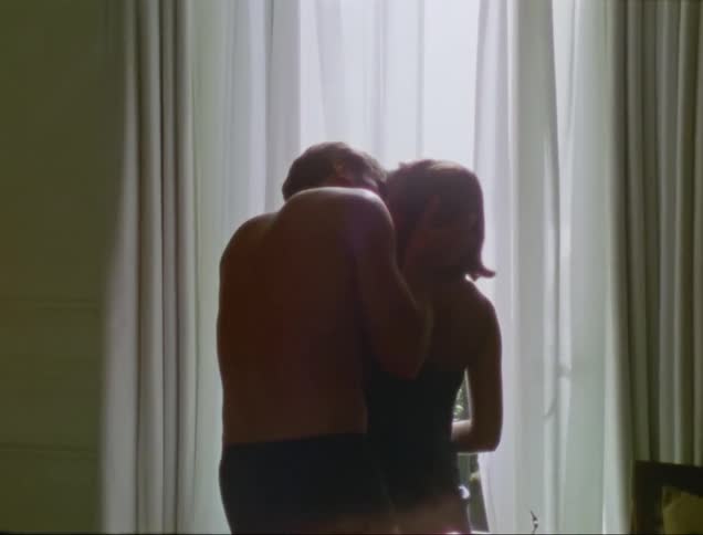 Man in only underwear giving his wife a kiss in front of a curtained window