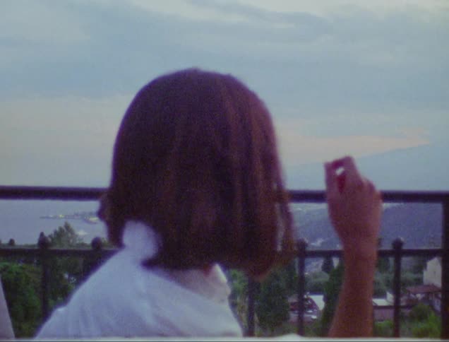 A woman sitting on the balcony of a building watching the city
