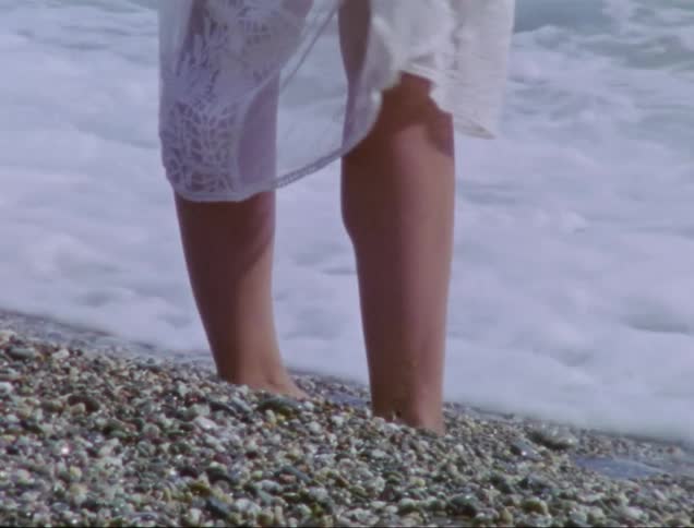 Woman in a white dress stands in the shoreline of a beach