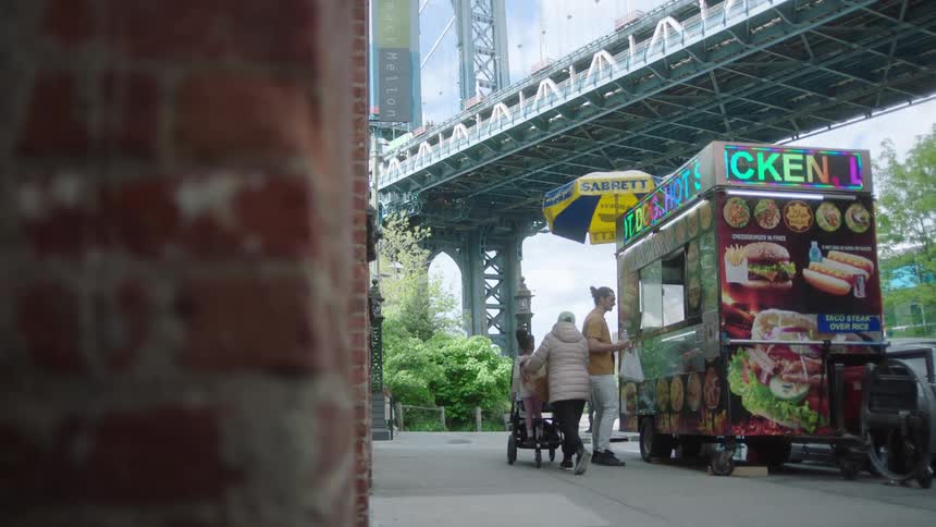 Man buying street food from a stand outdoors in a metropolitan neighborhood while other people and cars pass around during day time