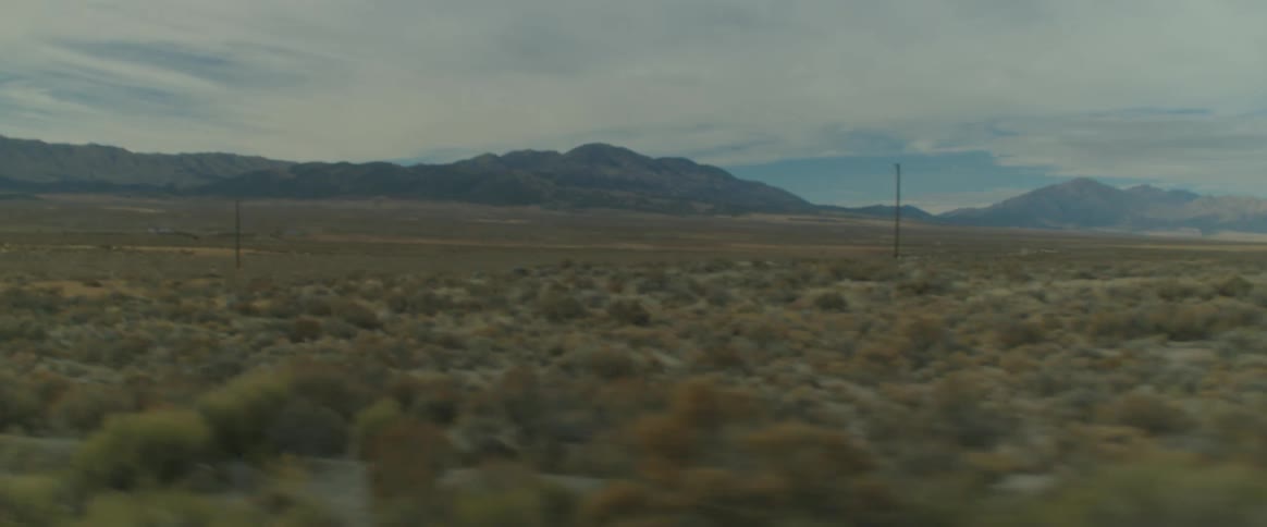 Vehicle drives down a road in the country with distant mountains in the background