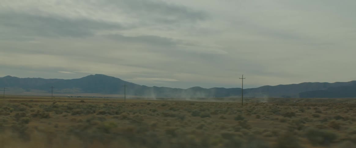 Dust floats through the air above field paralleling utility poles and mountains
