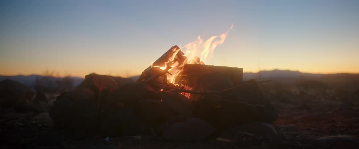 Flames rise as a bonfire burns and the sun sets