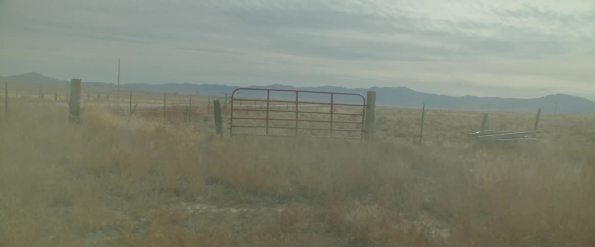 Dust passing through a pasture with a fence and a chain of mountains on the horizon
