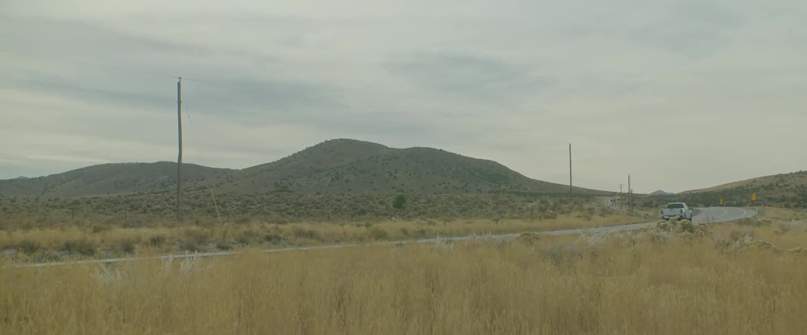 Truck passing on the road amidst fields and mountains on the horizon under a cloudy sky