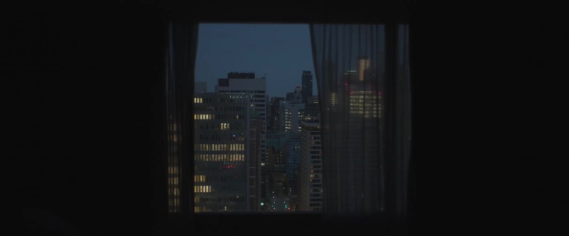 View from inside a dark room with a window overlooking a metropolis at night