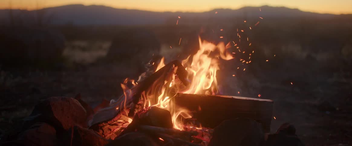 Close up of a campfire burns in the field casting a warm glow and creating a cozy atmosphere in the outdoor setting