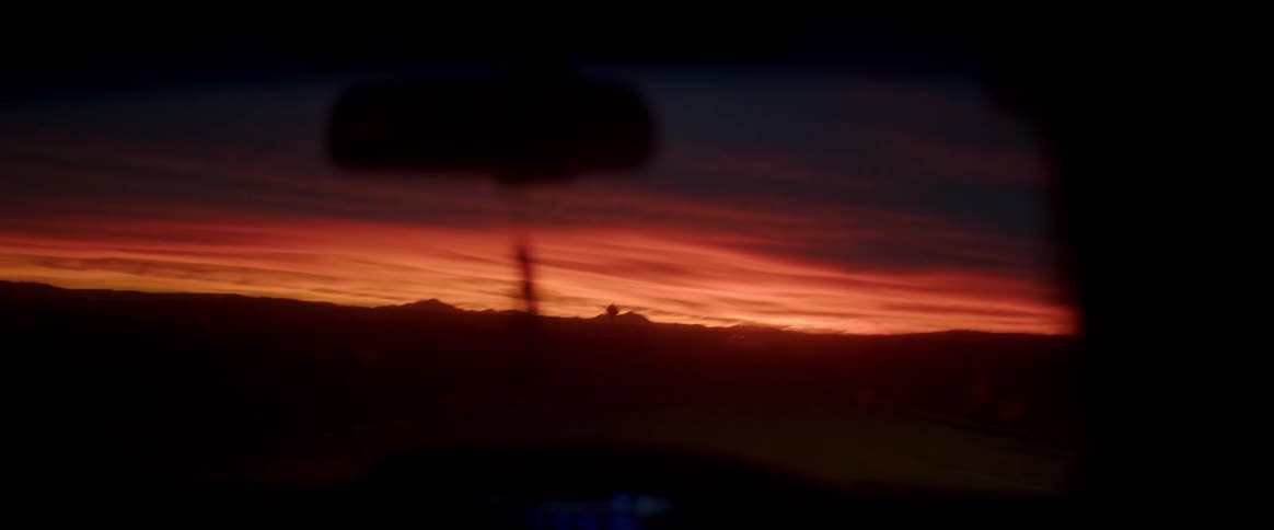 A person driving a car along the desert road during dusk