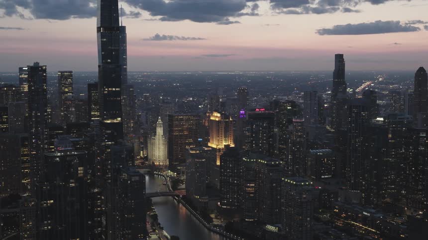 Aerial view of illuminated skyscrapers and tall buildings near a river in downtown area in the city