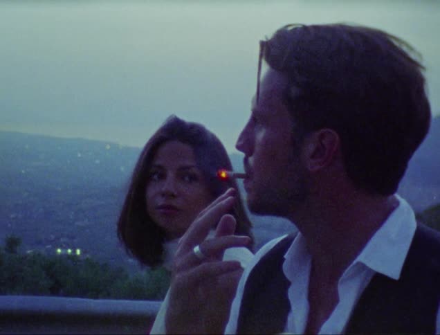 A man and woman share a cigarette outside