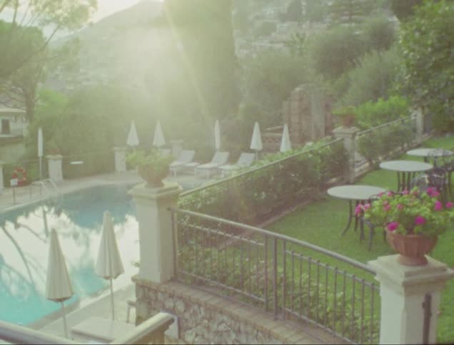 Man stands near tables overlooking swimming pool at resort at base of mountain town