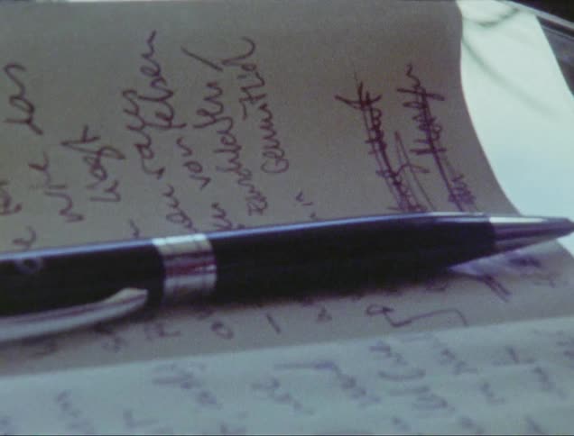 A person uses a pen to cross out a line of text in a small notebook