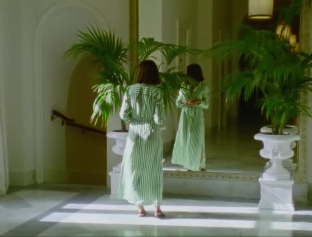 Woman wearing green dress walks towards her reflection in mirror