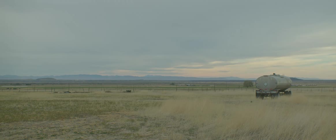 View of a pasture with a fuel tanker truck parked under a morning sky with clouds