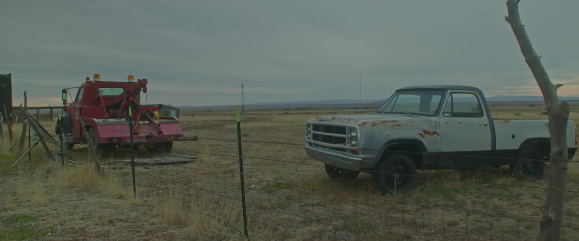 Tow truck next to a pickup truck both parked in a pasture