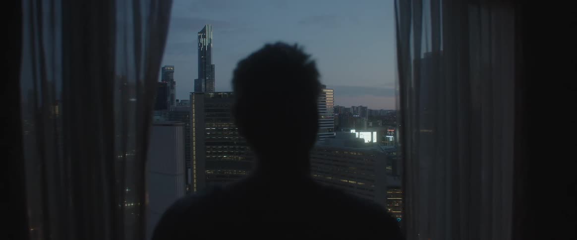 Silhouette of a man looking through the window at the view of a large city with several buildings