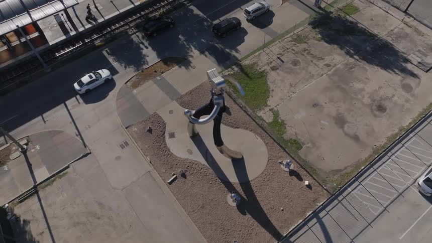 An abstract statue stands next to a street with cars driving by