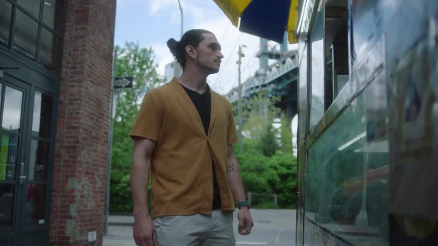A young man stands outside a food truck in a metropolitan area on a summer day