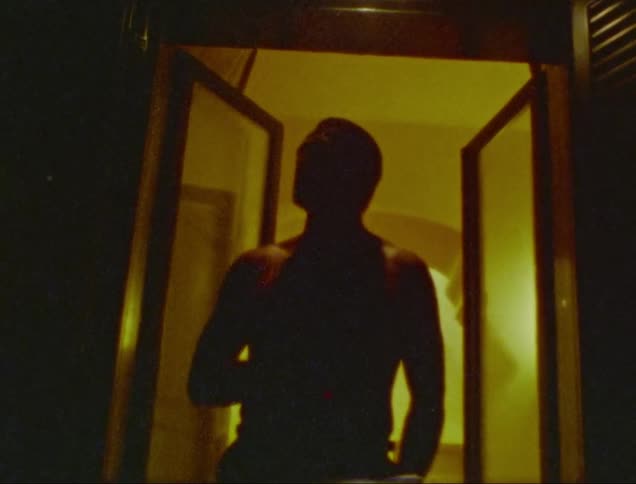 A man stands outside his house door at night smoking a cigarette