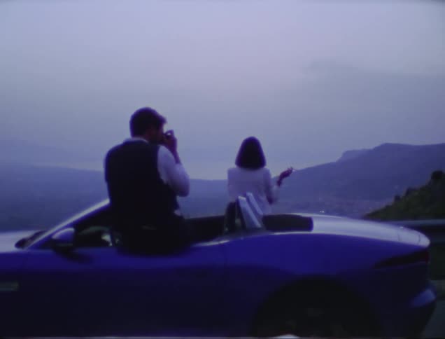 A clip of a male and female sitting on a blue car