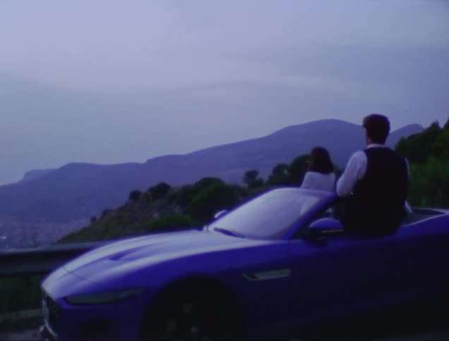 Couple with sports car look over town in foggy valley