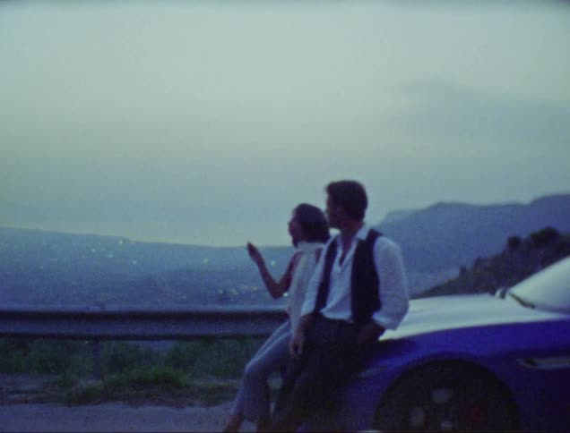 Couple sitting on the car hood smoking with a view of the city skyline